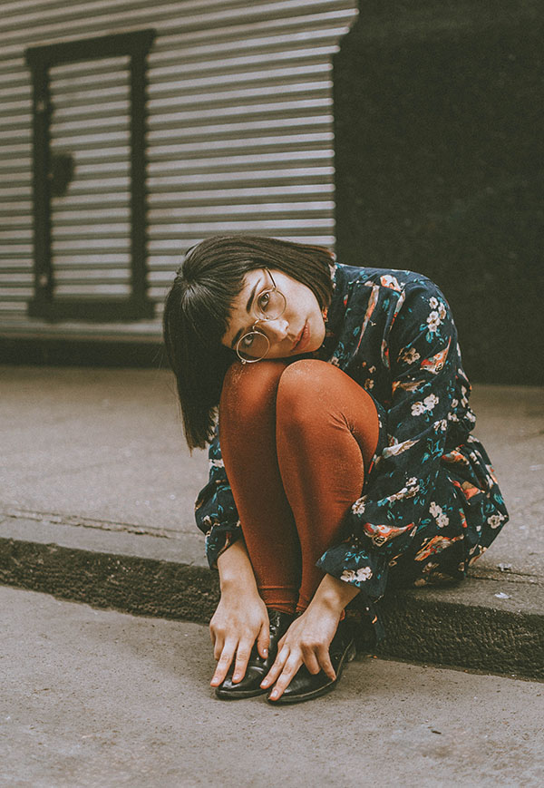 Mujer sensatada en bereda de calle mirando a cámara, vintage